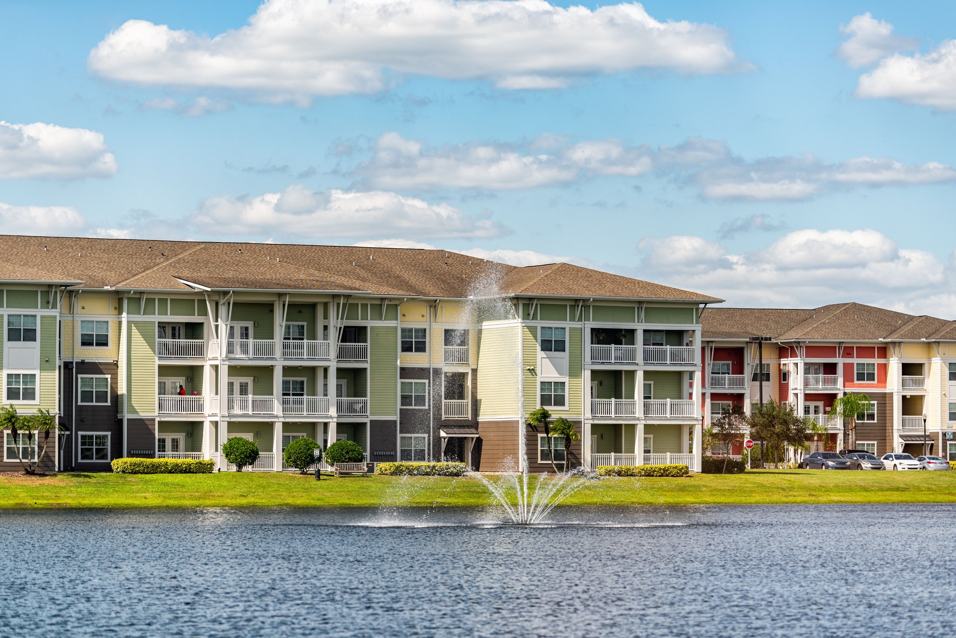 Orlando, Florida luxury lifestyle apartments buildings with three floors by lake water fountain in tropical city with blue sky clouds